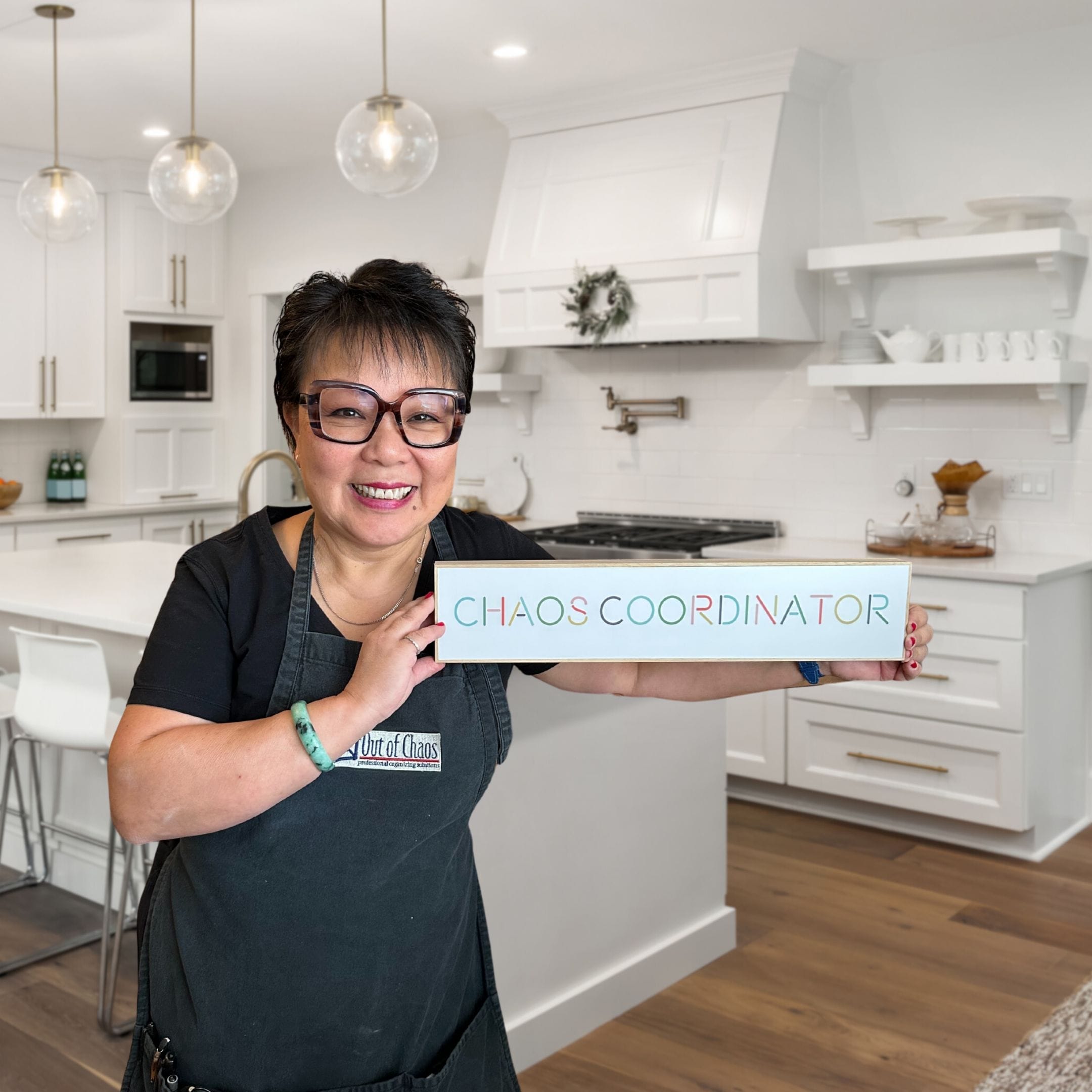 Linda Chu holding a sign that reads "Chaos Coordinator". Behind her is a nice kitchen.
