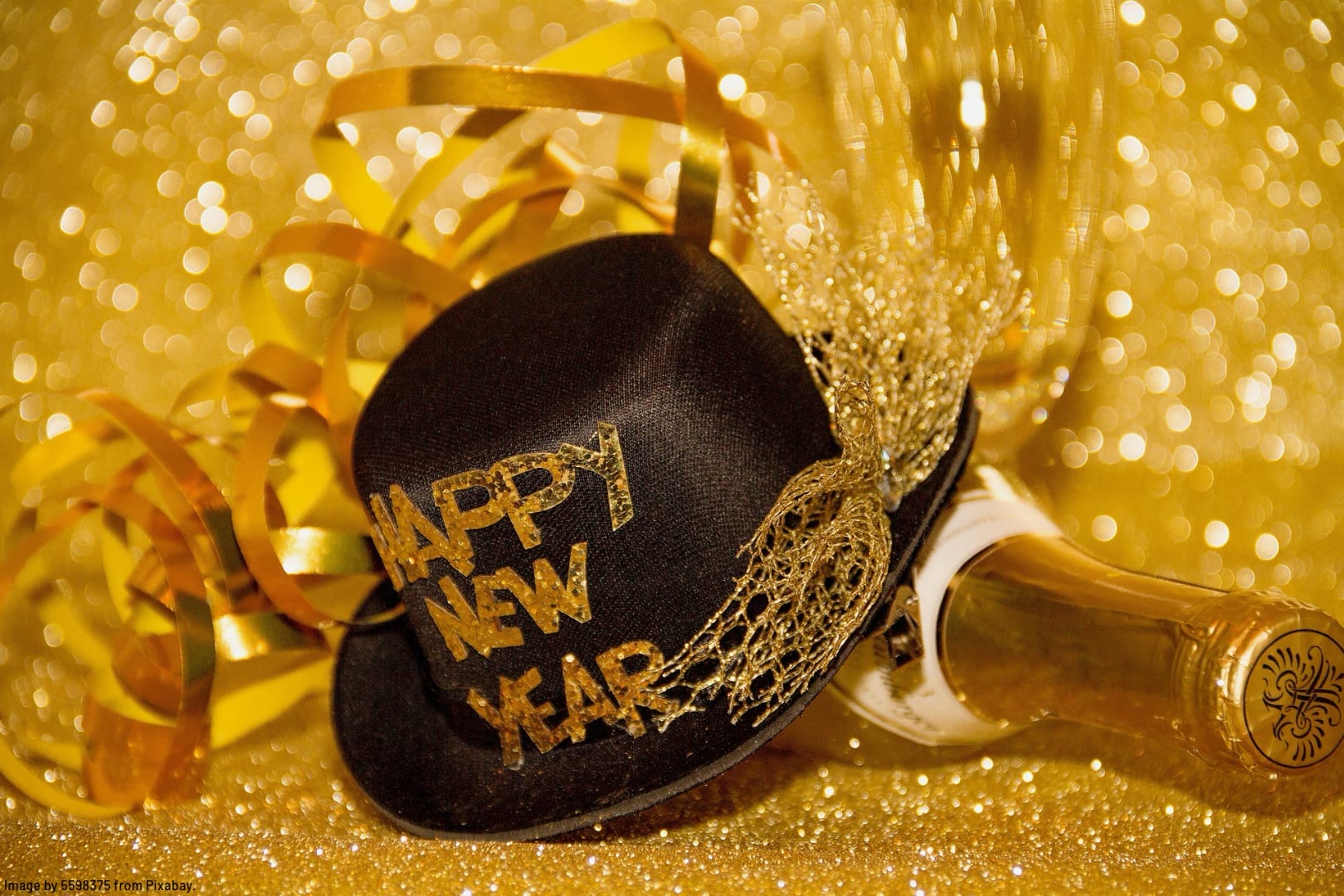 a top hat with the word Happy New Year on it beside a bottle of champagne on gold glitter with a gold background