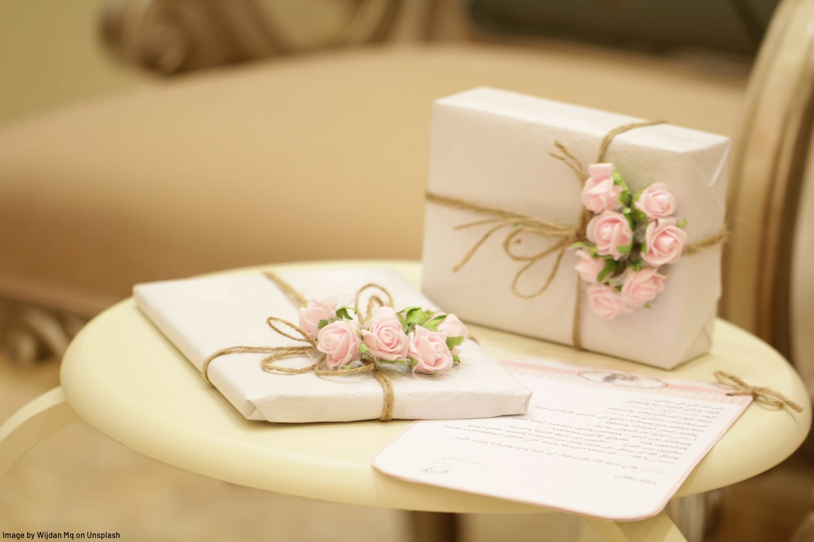 gifts on table wrapped in white paper tied with string and pink flowers added for decoration