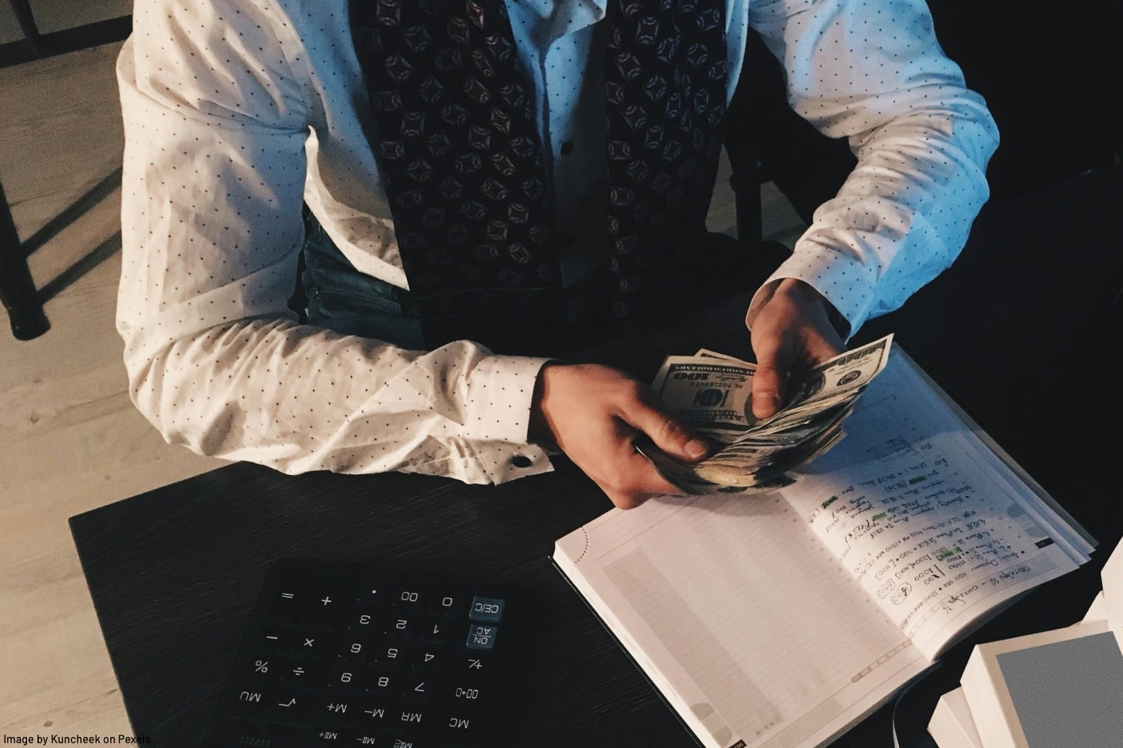 bookkeeper sitting at desk with computer, calculator, notebook, counting money