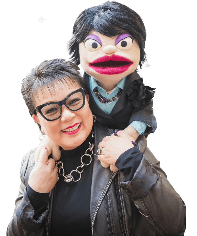Linda Chu is smiling and holding a puppet on her shoulders. The puppet has dark hair and a suit.