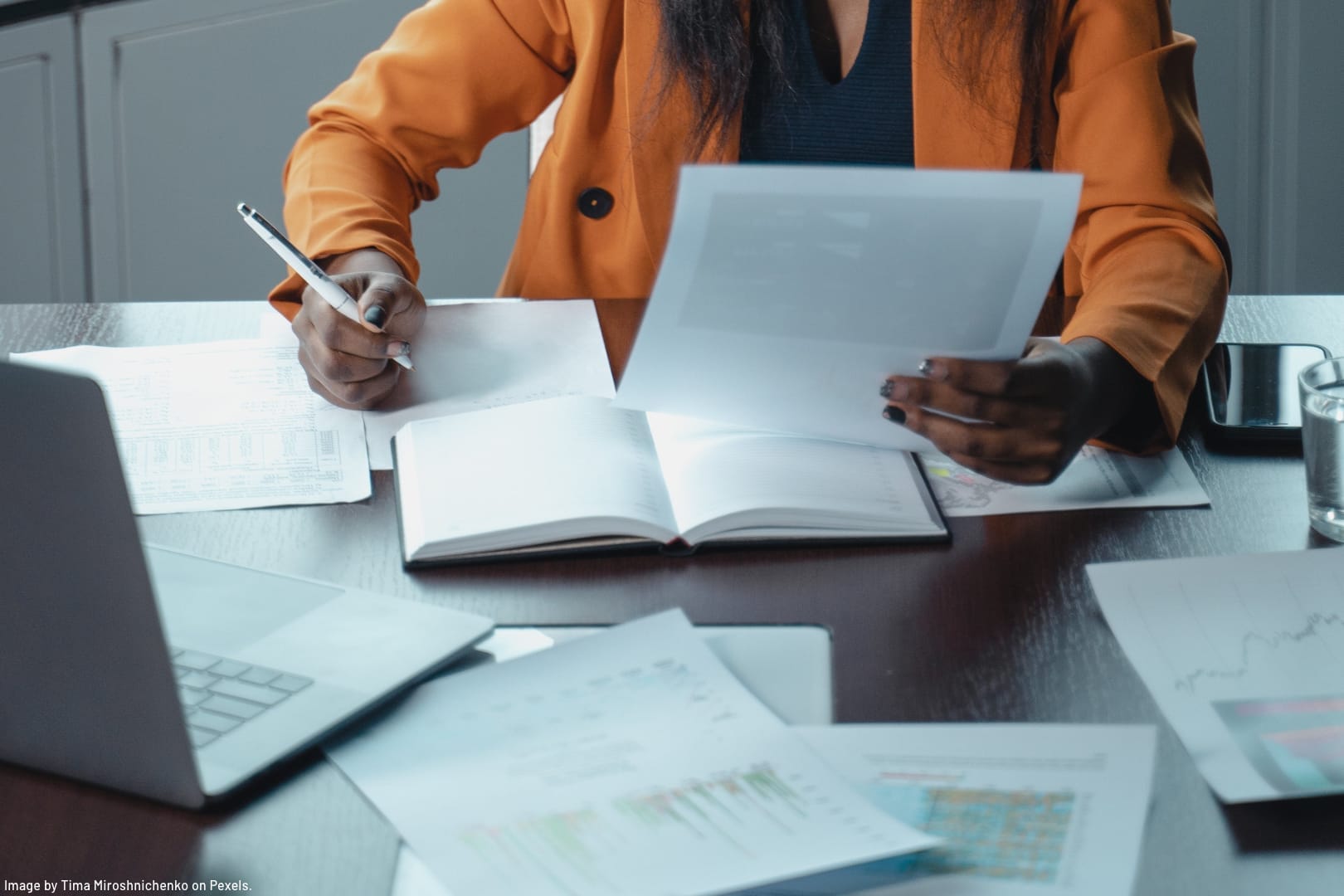 woman of colour wearing orange jacket sitting at a desk studying business