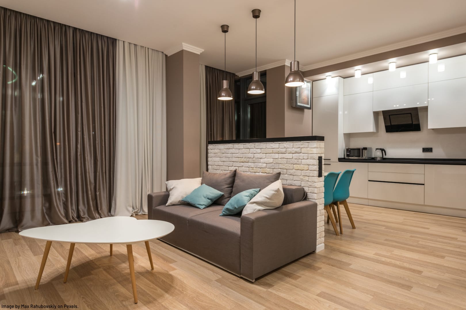 a tidy, minimalist home showing a sofa and coffee table with a brick wall behind and a galley style kitchen in the background