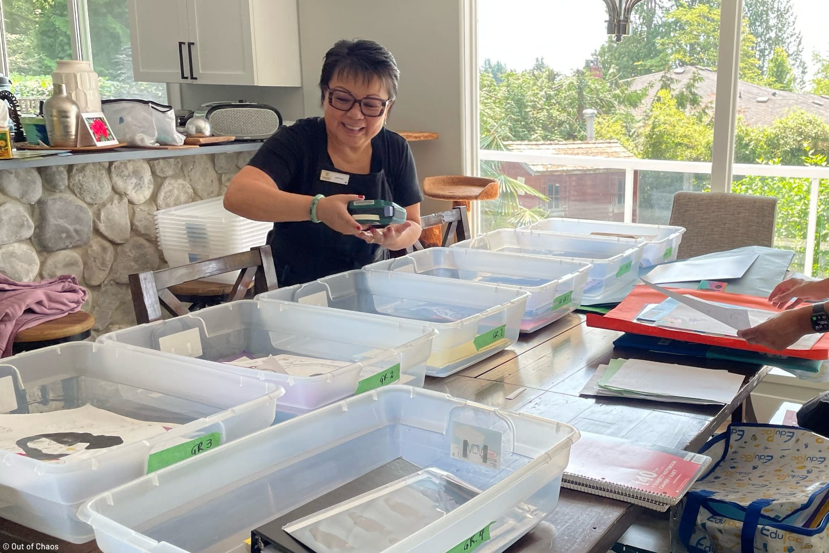 Linda Chu sorting a client's school memorabilia into clear totes on a dining table