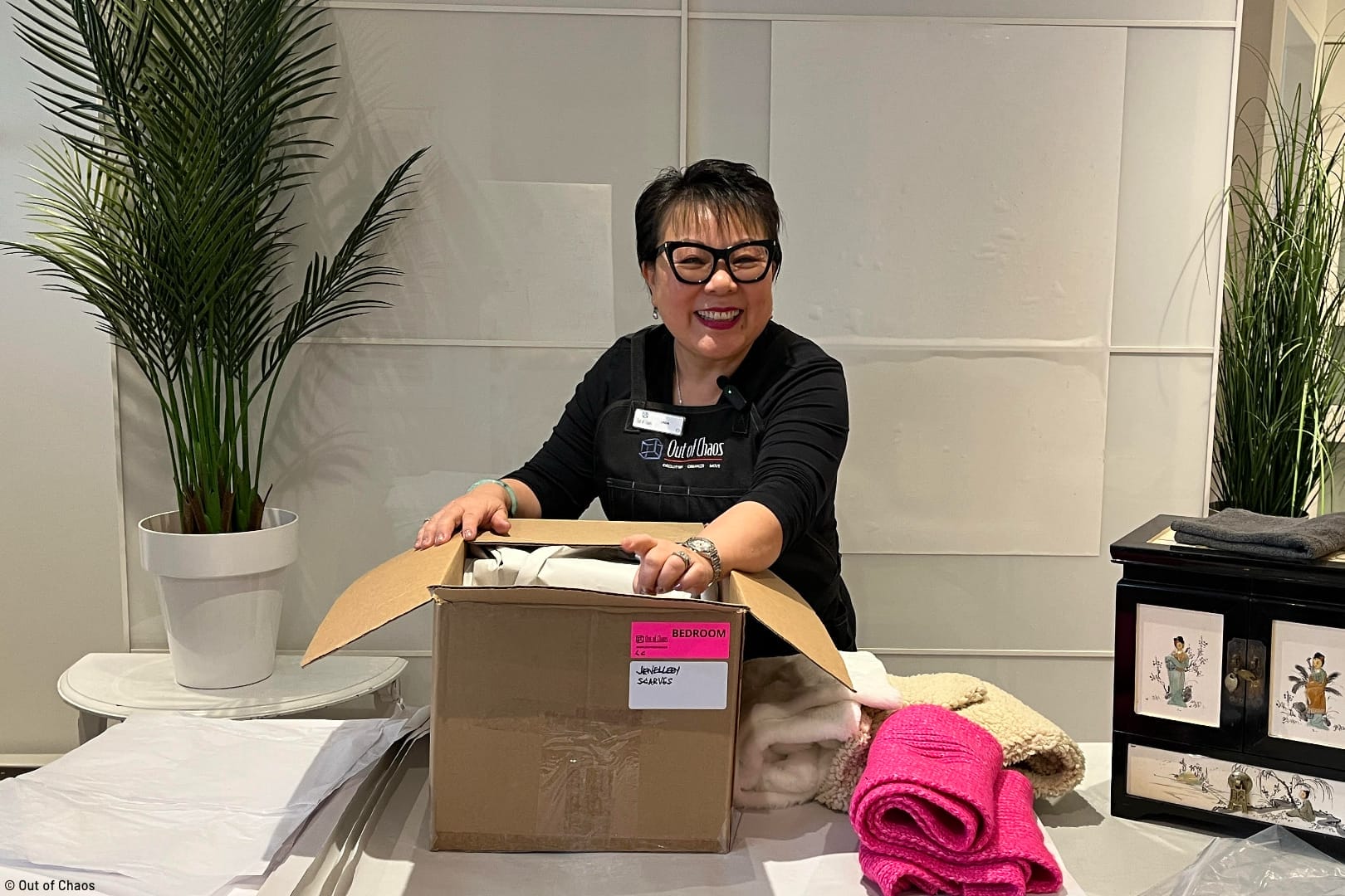 Linda Chu, founder of Out of Chaos smiling at the camera while packing moving box during their move management services