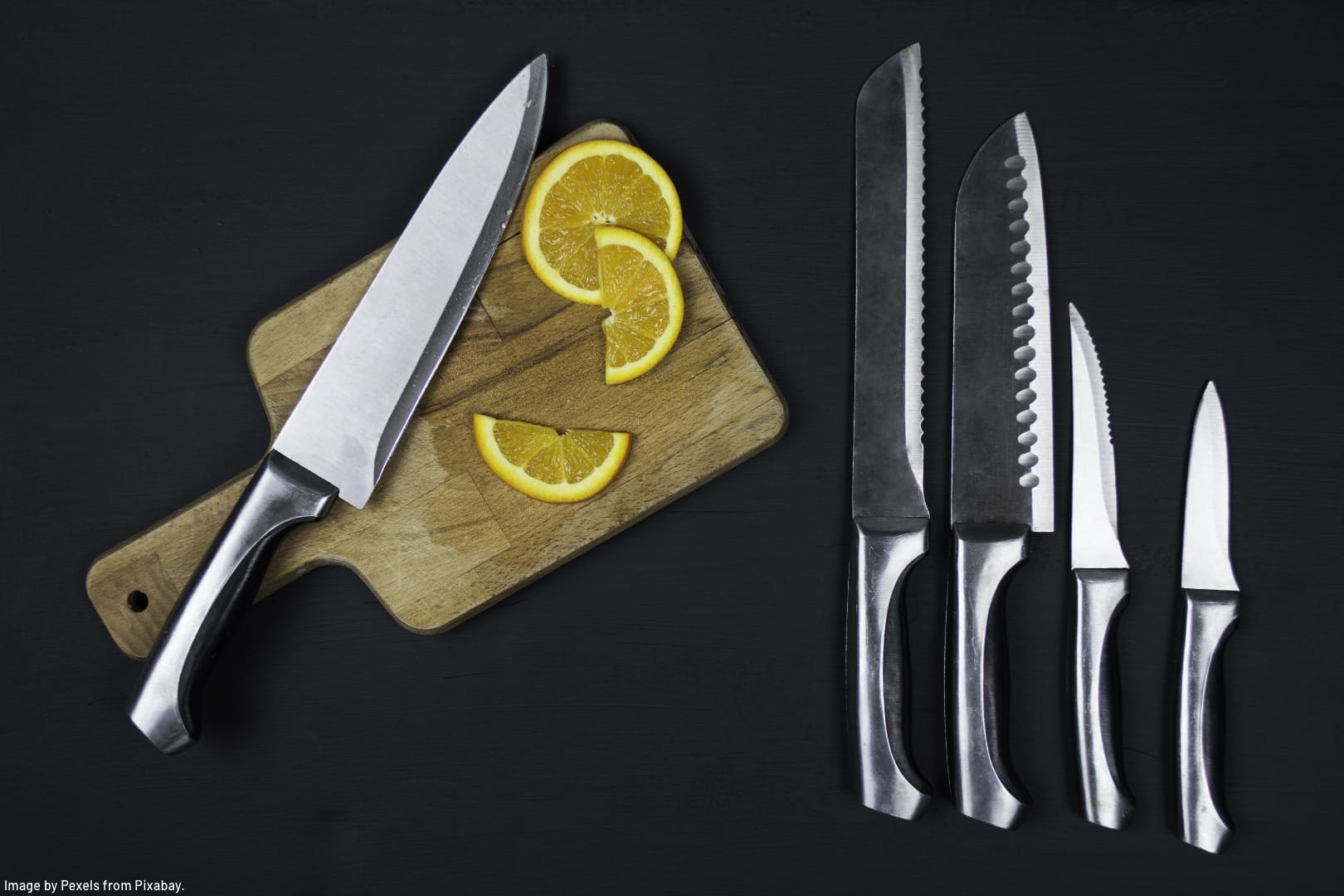 chef's knife on a bamboo cutting board with slices of lemon and other knives from the set lined up neatly beside it