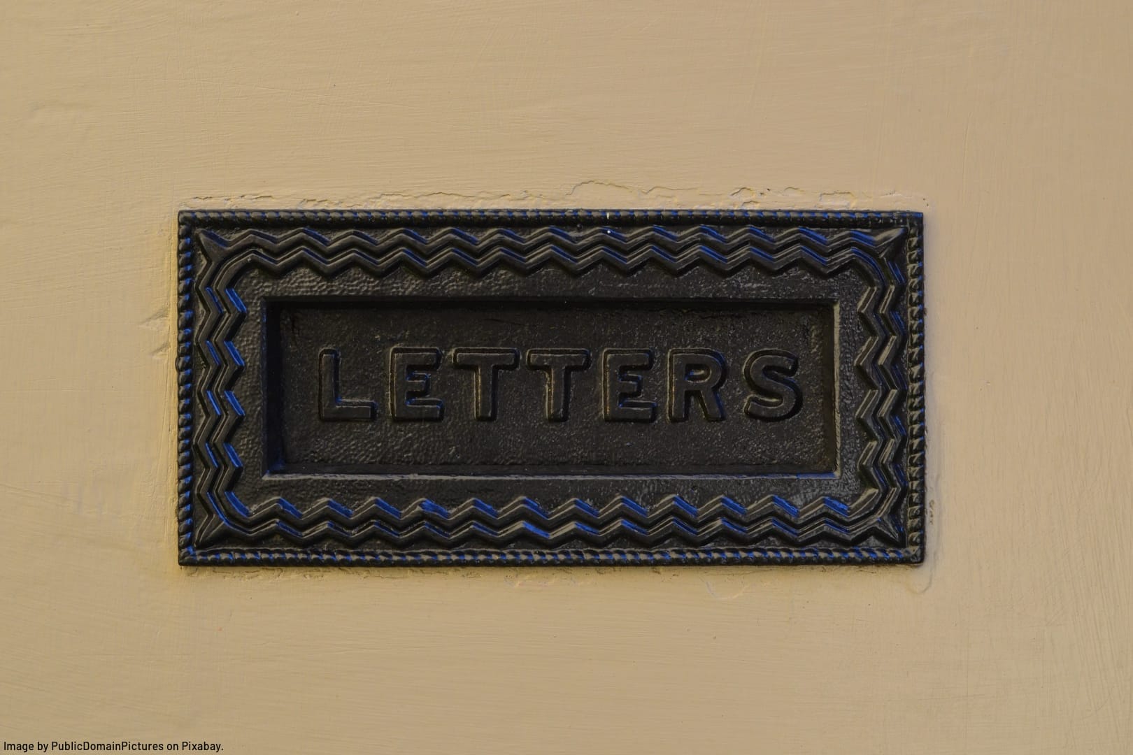 cast iron mail slot in wall with the word LETTERS stamped on it