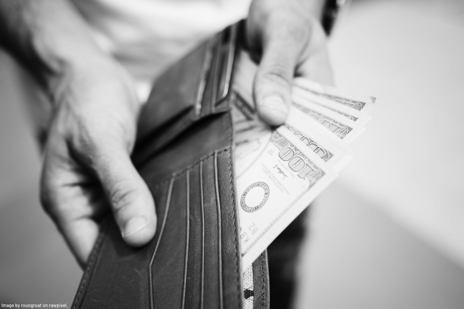 grey scale photo of hands pulling money out of leather wallet